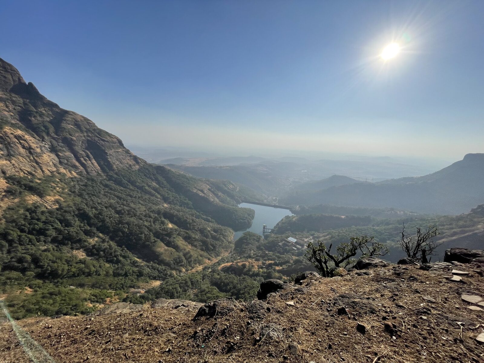Sun shining over a hazy mountain valley with a reservoir far below a rocky ledge