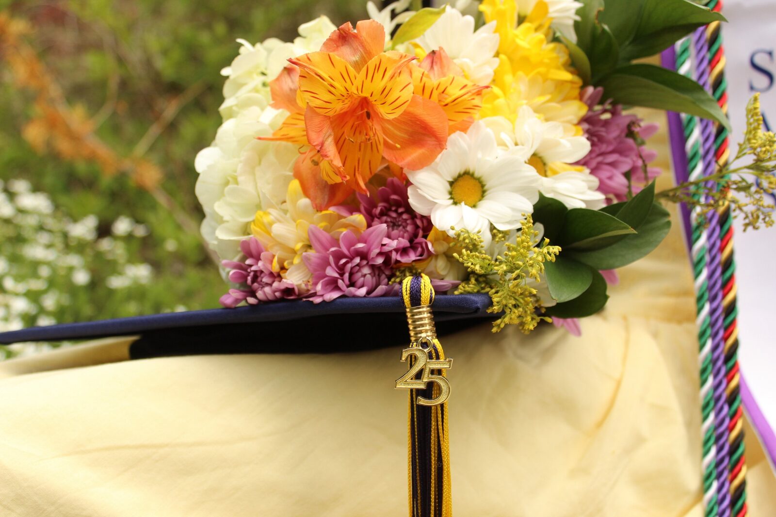 A graduation cap crowned with a bouquet, a gold 25 charm hanging from the tassel