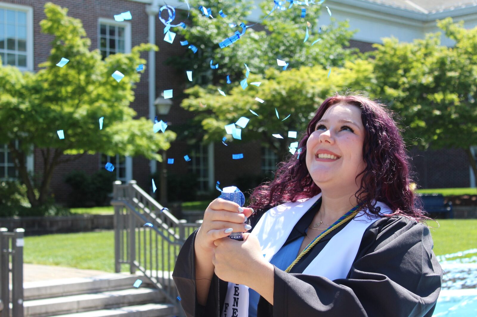 Maddie, a graduate with purple hair, laughing as blue confetti bursts overhead